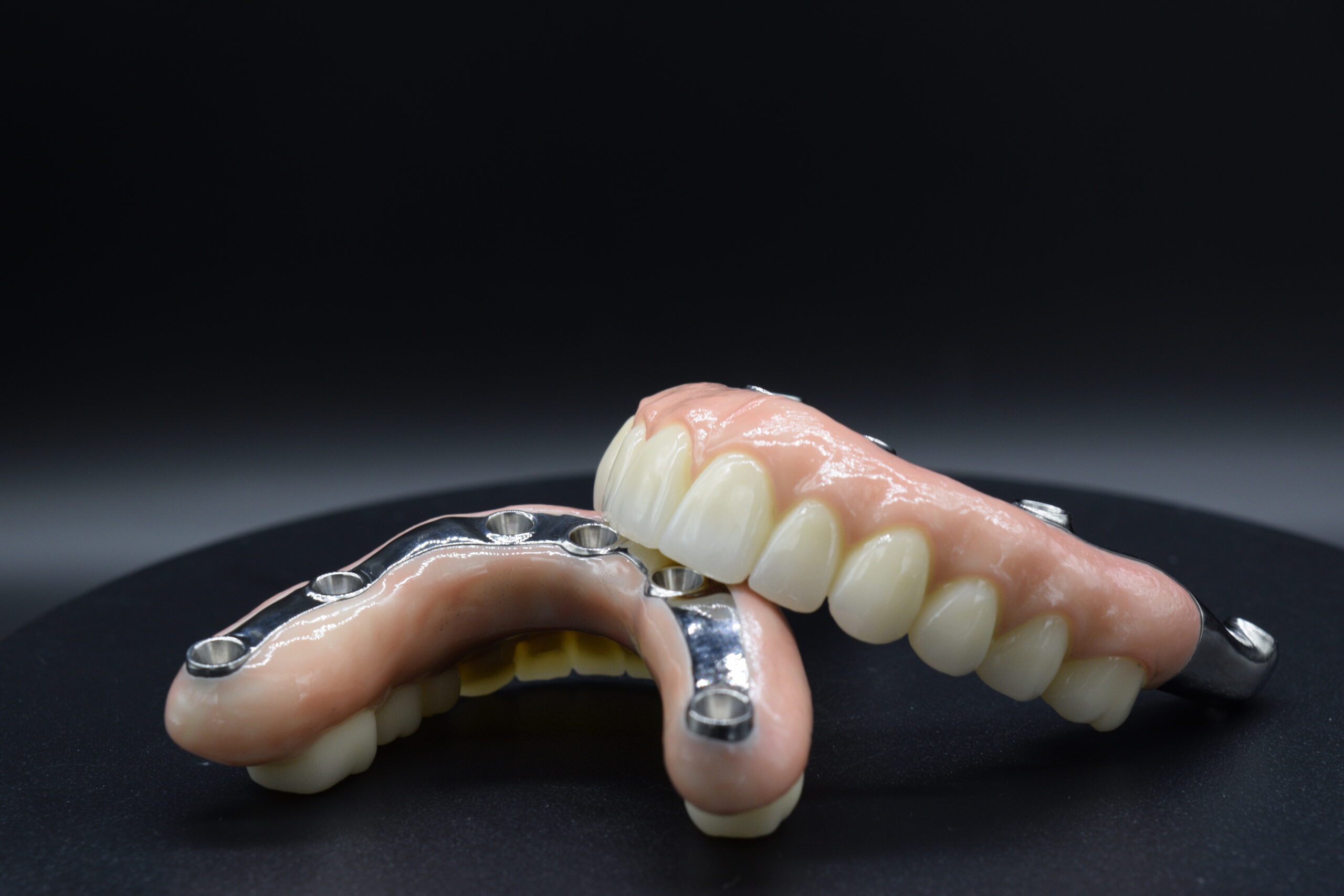 Two Sets of Dental Implants With Realistic Teeth and Metal Connectors Displayed on a Black Surface, Against a Dark Background, Highlighting Dental Technology.