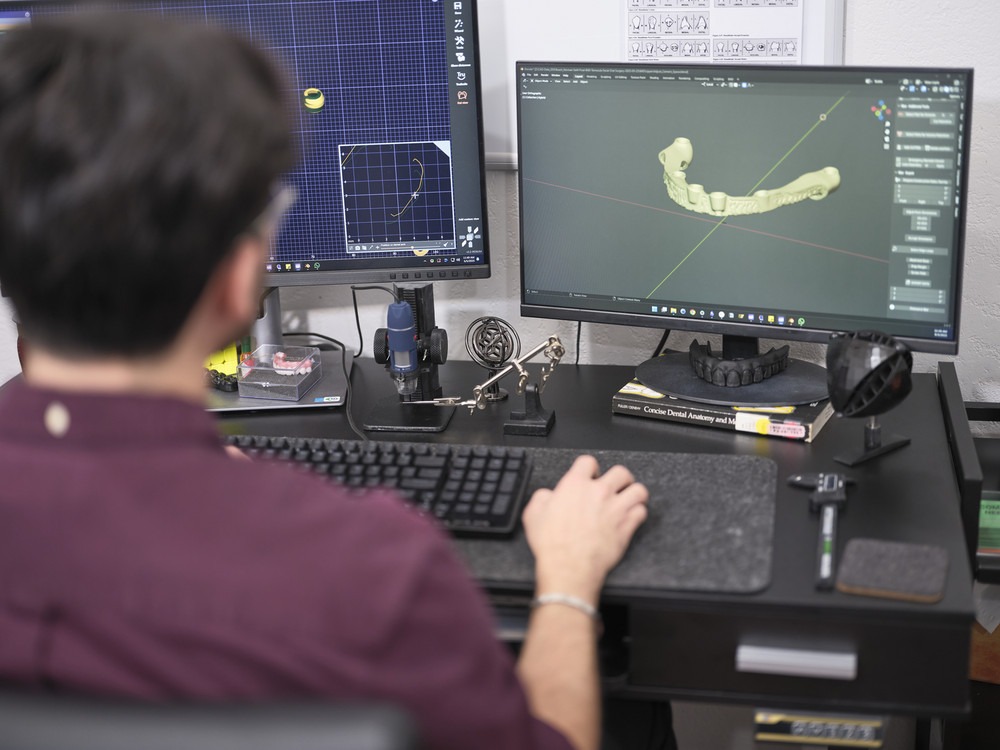 A Man Focused On a Computer, Working With Two Monitors Displaying Various Applications.